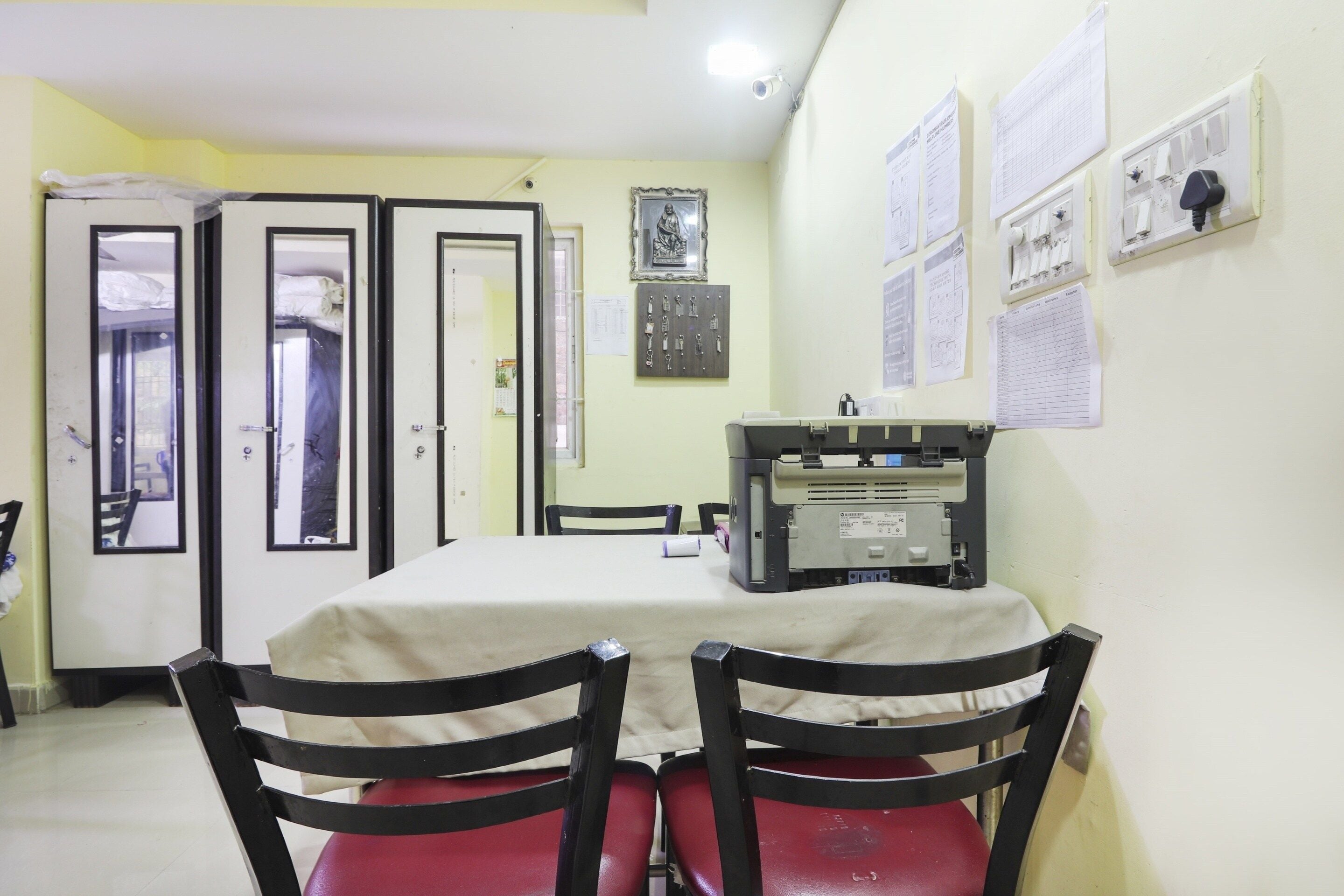 Una habitación con una mesa, sillas, una impresora y varios documentos en la pared.