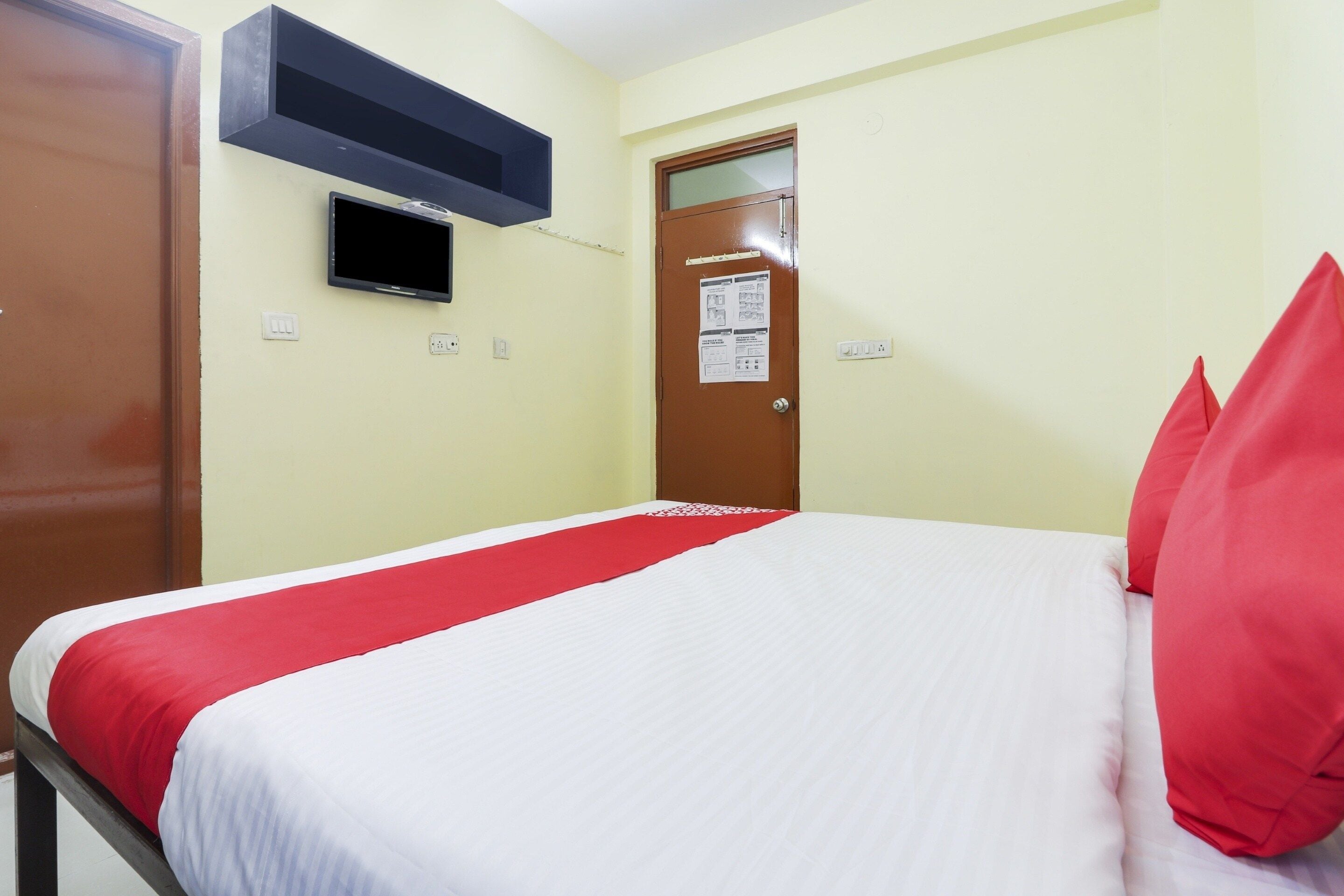 Habitación de hotel con cama, televisor montado en la pared, puerta con un aviso y un enchufe.