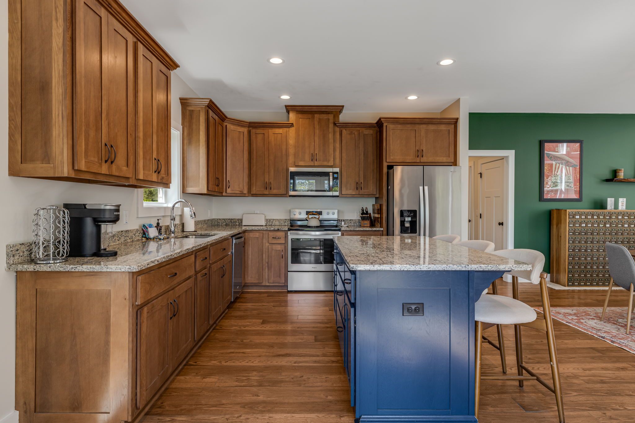 Une cuisine moderne avec des meubles en bois, un îlot central bleu, des appareils électroménagers en acier inoxydable et un mur d’accent vert.