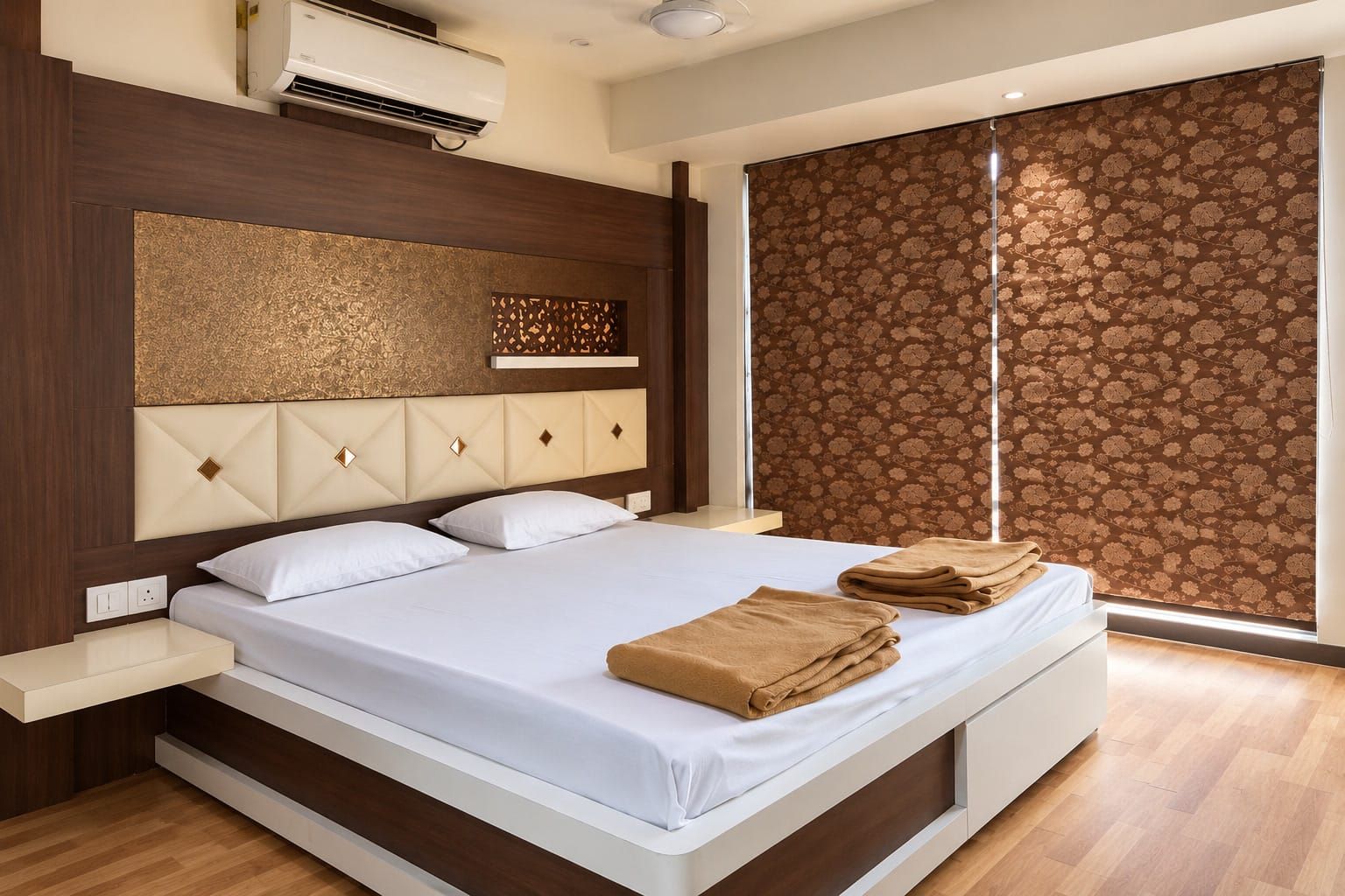 A modern hotel room with a large bed, a headboard with a geometric pattern, a window with a floral blind, and a wooden floor.
