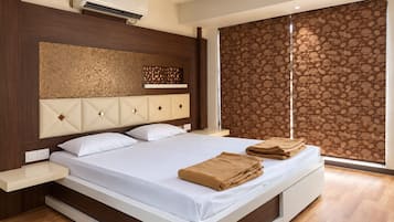 A modern hotel room with a large bed, a headboard with a geometric pattern, a window with a floral blind, and a wooden floor.