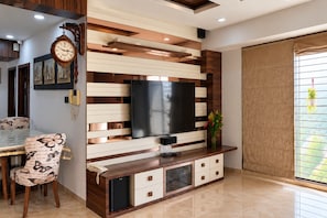 Una sala moderna con televisor de pantalla plana, pared de paneles de madera y blanco, un comedor con una silla estampada de mariposas y un refrigerador pequeño.