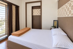 Une chambre d’hôtel avec un lit, une fenêtre avec des rideaux, une porte et une petite table de chevet sur laquelle se trouve une plante.