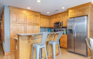 A kitchen with wooden cabinets, stainless steel appliances, and a bar stool. - Beach Club 125: 2  BR, 2  BA Condominium in Tybee Island, Sleeps 6 (Tybee Island)