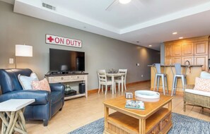 A living room with a sofa, TV, and a dining area with chairs and a table. - Beach Club 125: 2  BR, 2  BA Condominium in Tybee Island, Sleeps 6 (Tybee Island)
