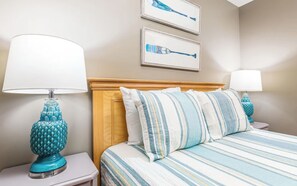 A hotel room with a bed, two nightstands, a wooden headboard, and two wall-mounted lamps. - Beach Club 125: 2  BR, 2  BA Condominium in Tybee Island, Sleeps 6 (Tybee Island)