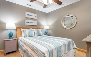 Ein Schlafzimmer mit einem Bett, zwei Nachttischen, einem Deckenventilator, einem an der Wand befestigten Spiegel und zwei gerahmten Bildern.