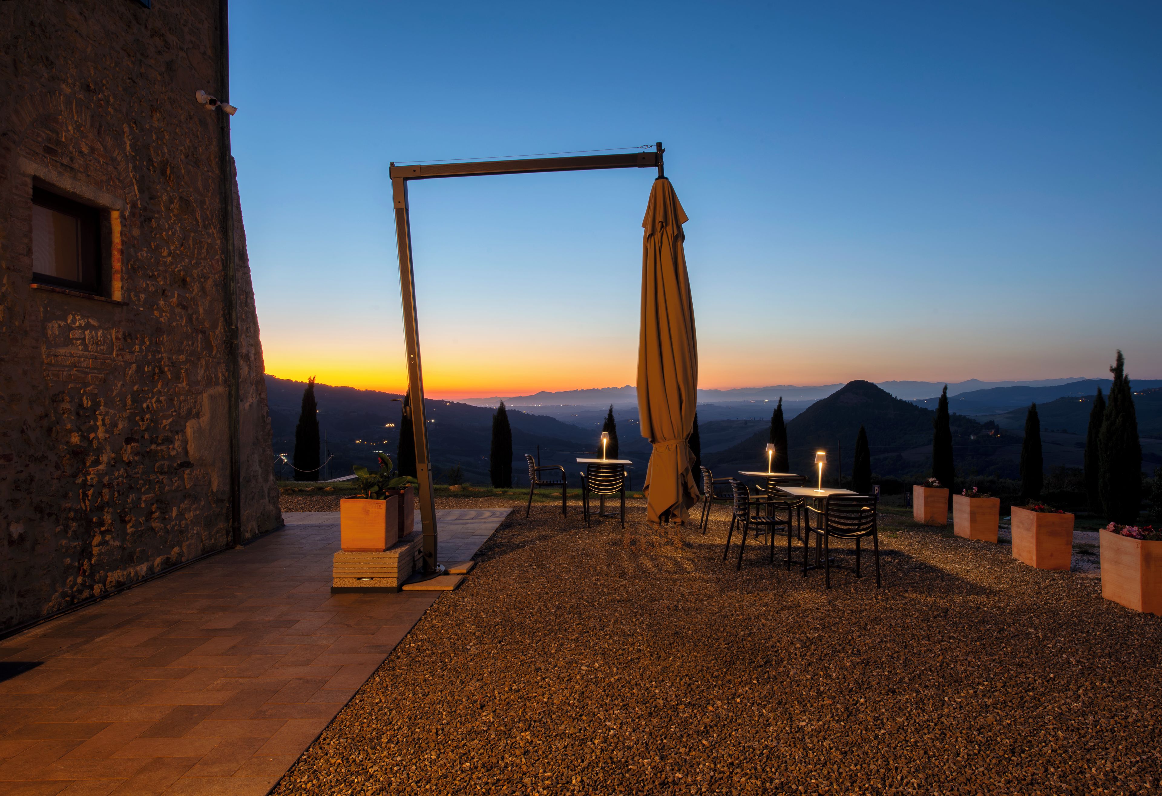 An outdoor seating area with tables and chairs, a swing set, and a view of the mountains at dusk.