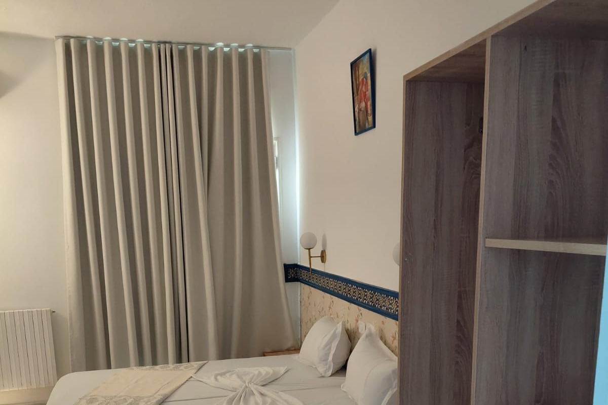Quarto com cama, mesa de cabeceira, guarda-roupa e janela com cortinas.