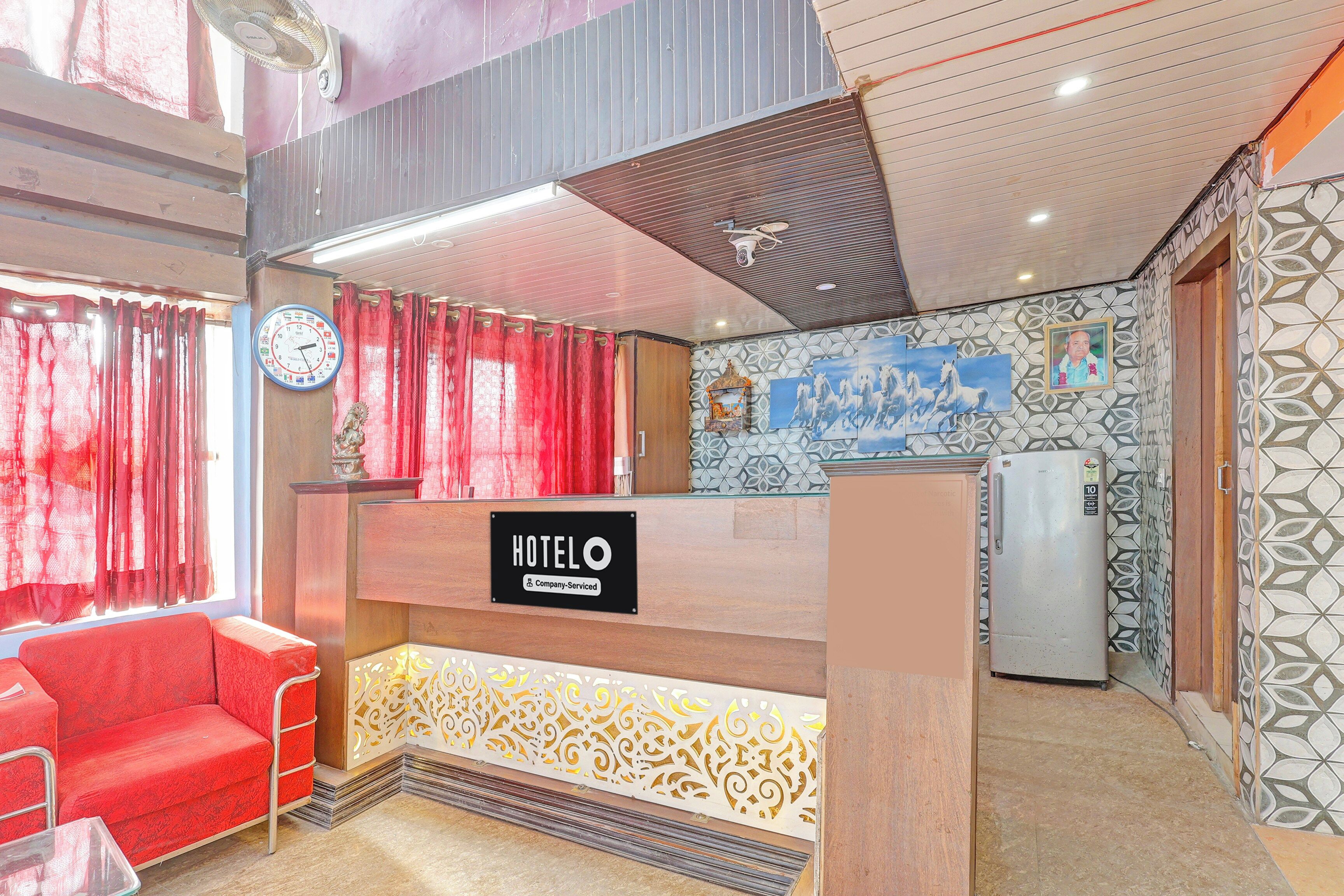 Uma área de recepção de hotel com um relógio, cortinas vermelhas, um balcão de atendimento e um frigorífico.