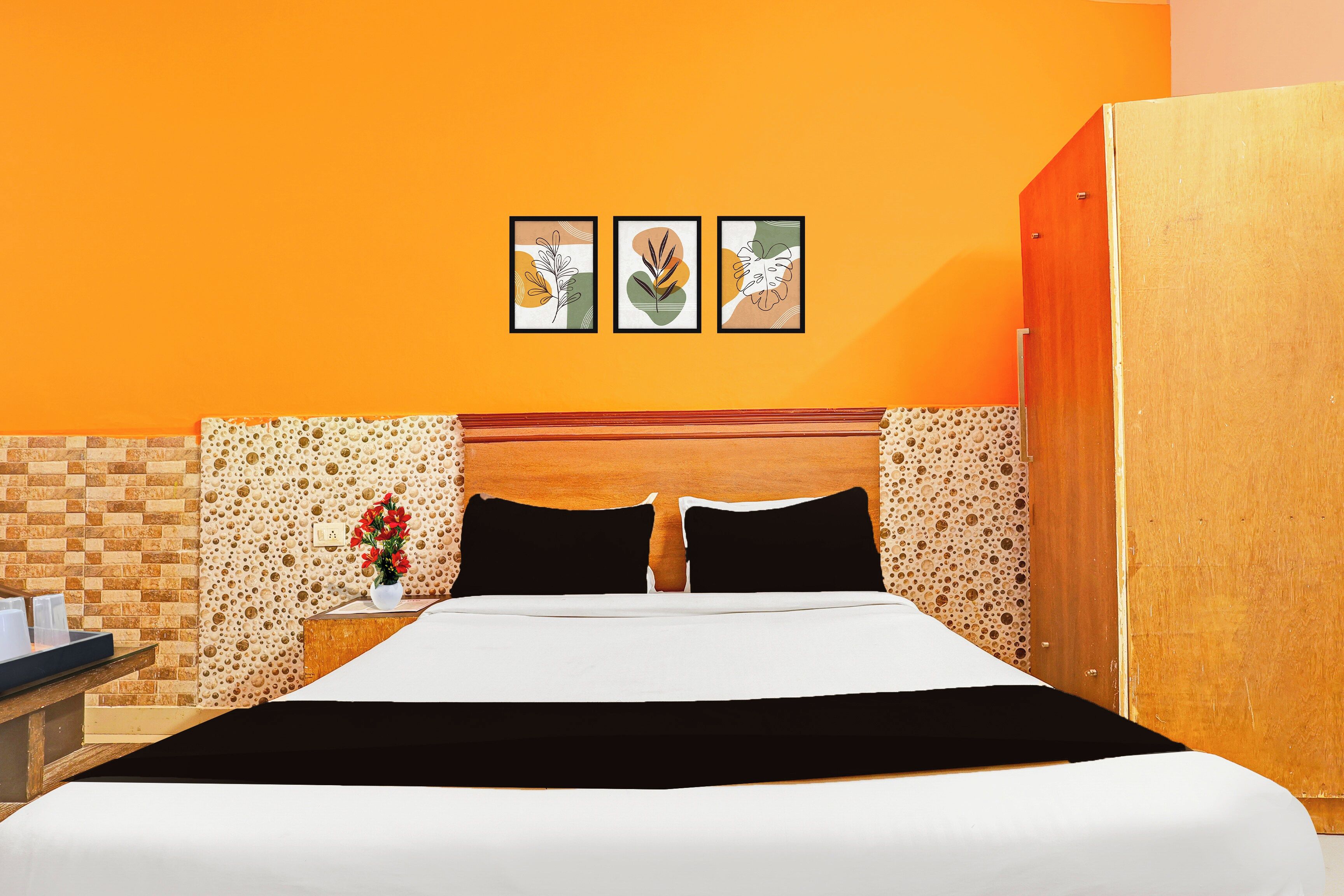 A hotel room with a bed, a nightstand, a vase with flowers, and three framed pictures on the wall.