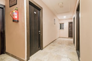 A corridor with a fire extinguisher mounted on the wall, a door with a number plate, and a window with a view. - Hotel O Raipur City Center (Raipur)
