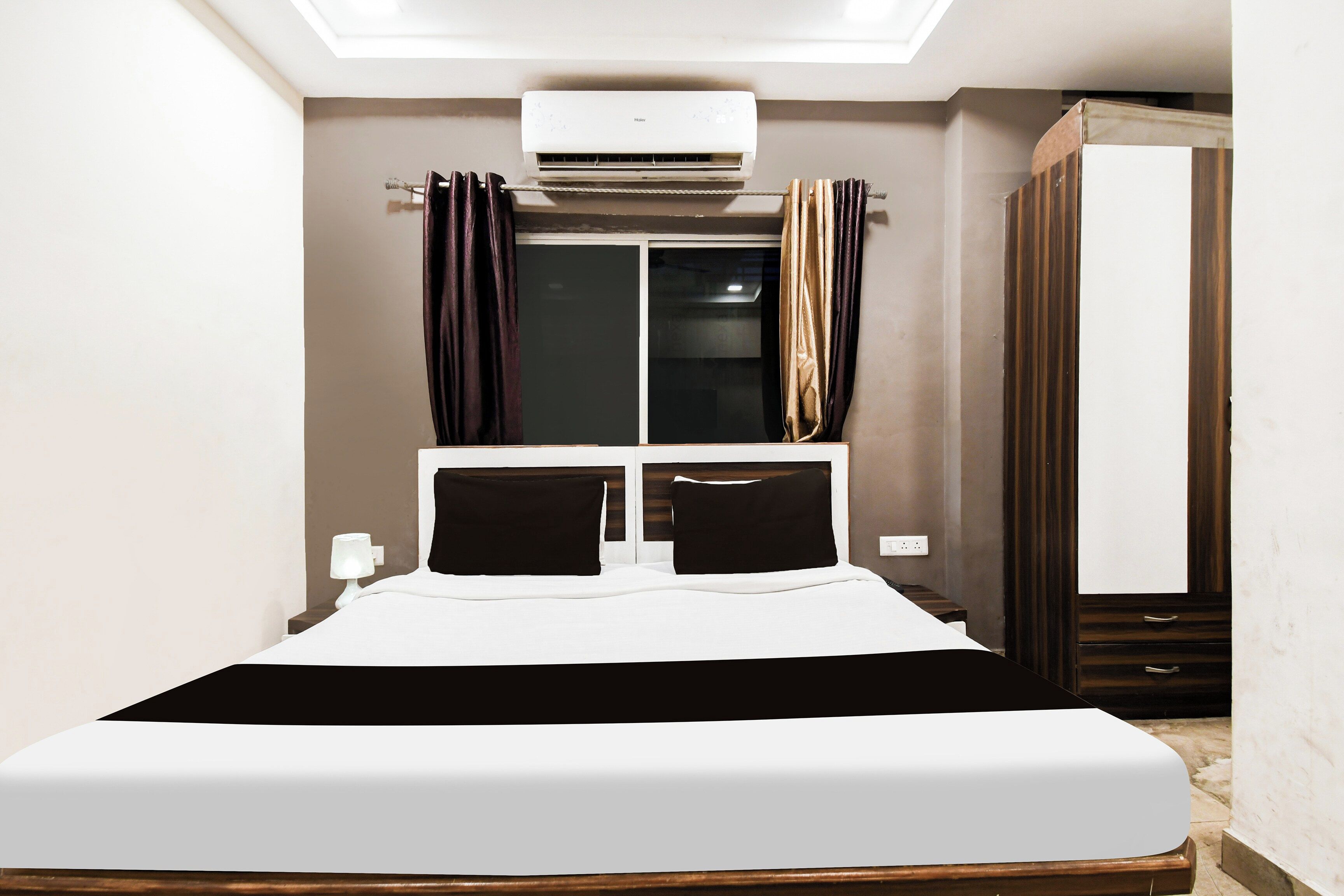 Una habitación de hotel con cama, aire acondicionado, armario y ventana con cortinas.