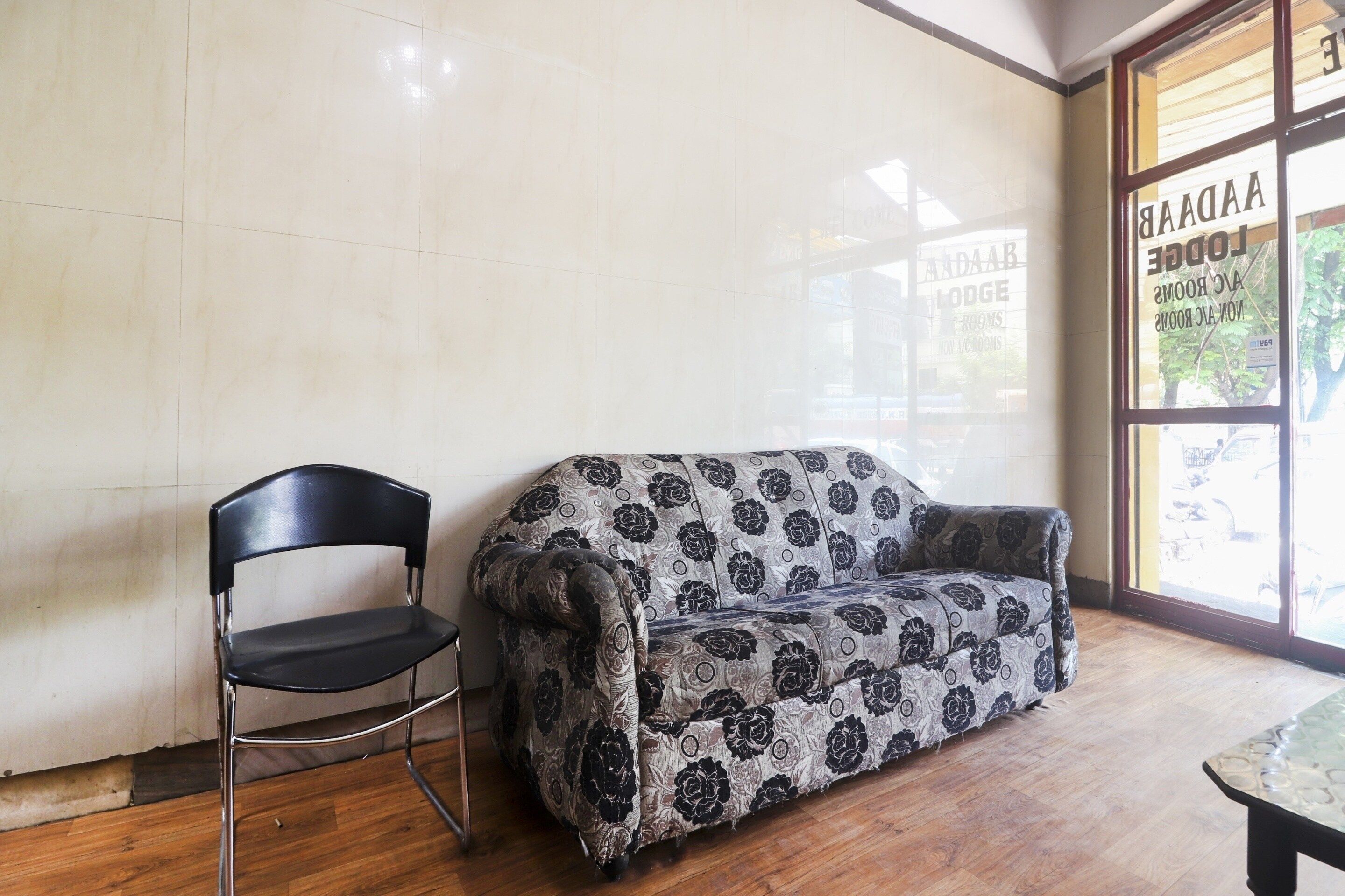 Una habitación con un sofá estampado, una silla negra y suelo de madera.