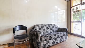 Una habitación con un sofá estampado, una silla negra y suelo de madera.