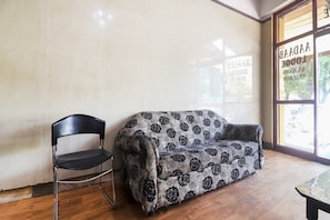 Una habitación con un sofá estampado, una silla negra y suelo de madera.