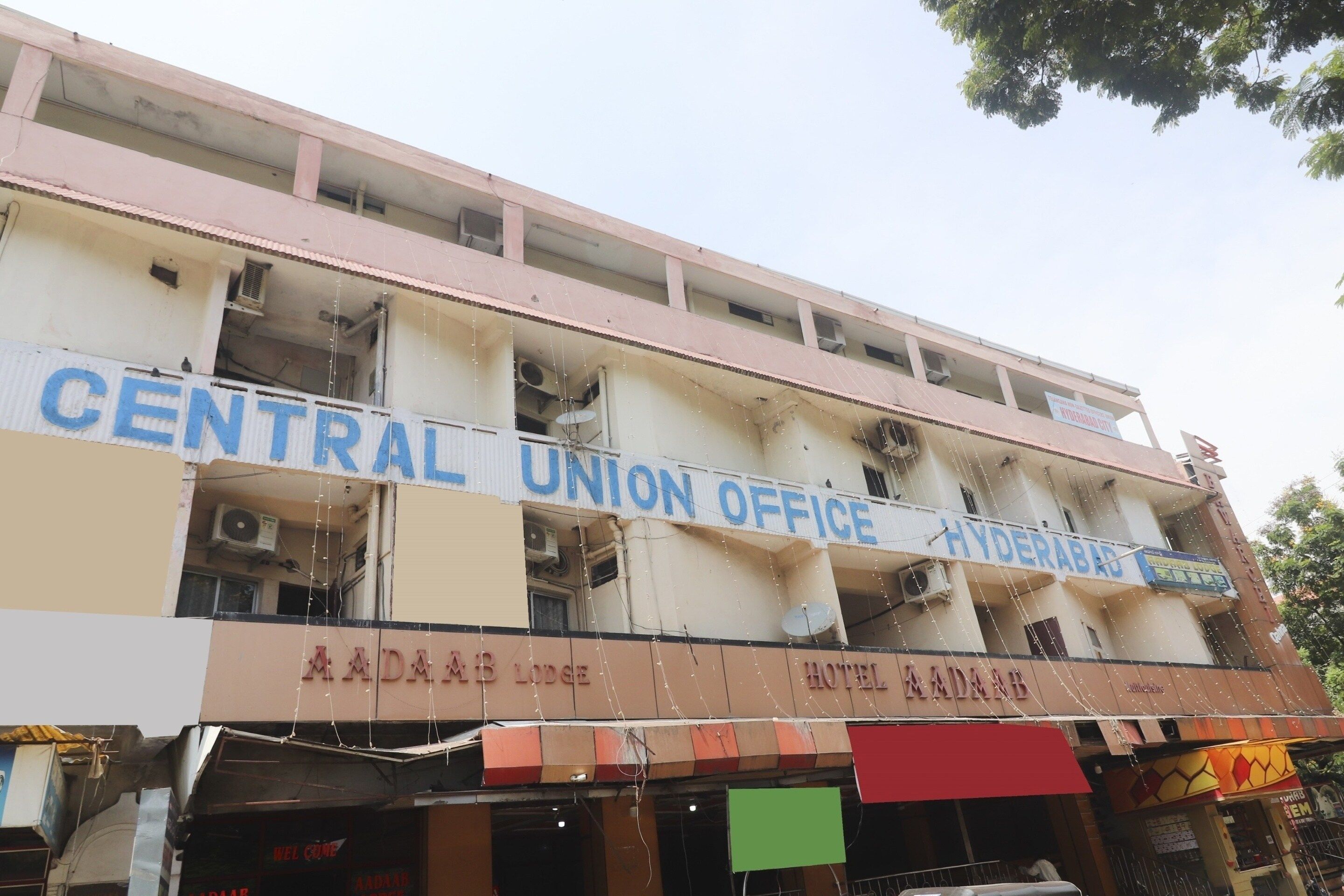 Een meerhoog gebouw met borden voor 'Central Union Office Hyderabad City' en 'Aadaar Lodge Hotel Ramnagar'.