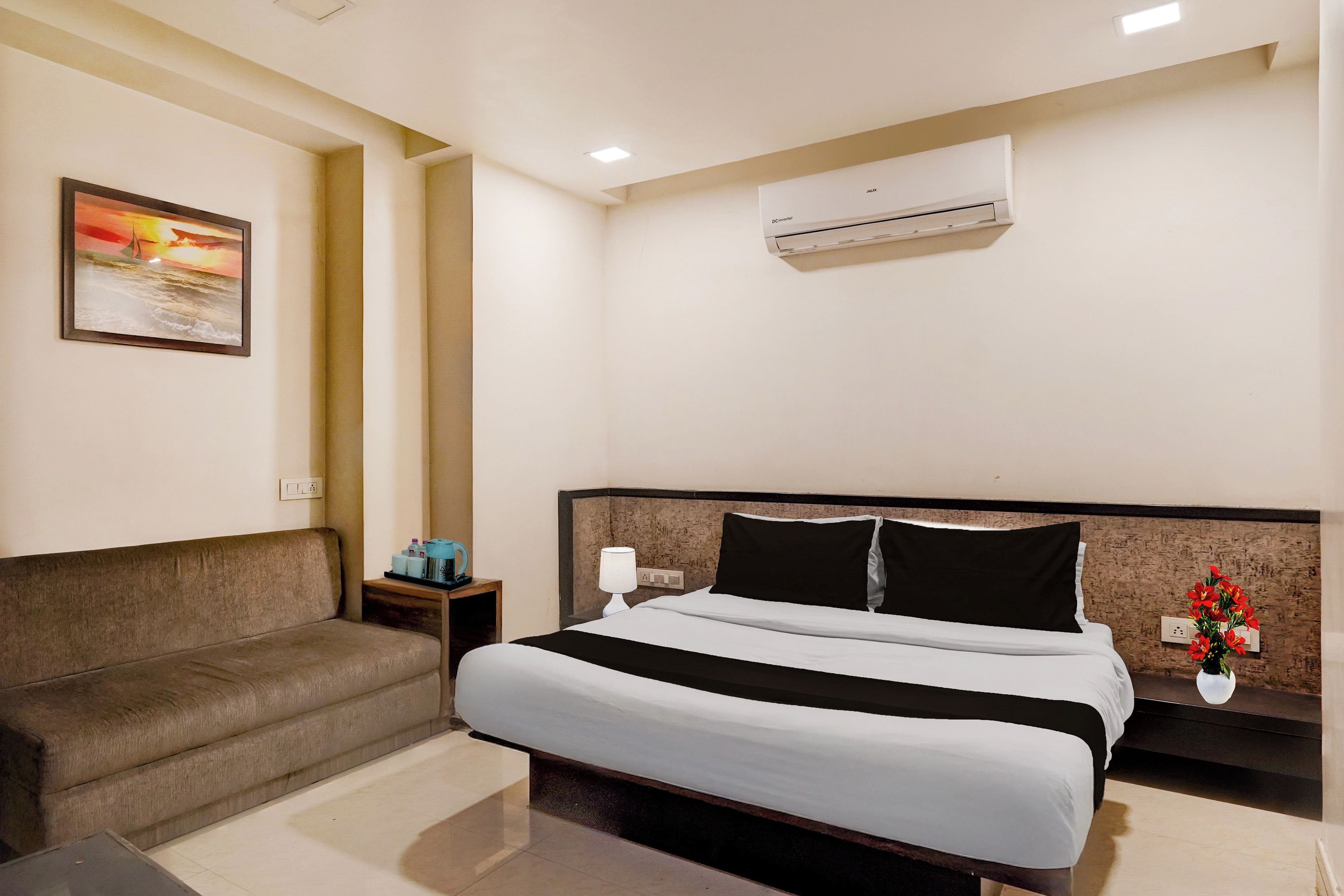 Habitación de hotel con cama, sofá, aire acondicionado, un cuadro y un florero con flores.