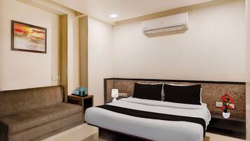 Habitación de hotel con cama, sofá, aire acondicionado, un cuadro y un florero con flores.