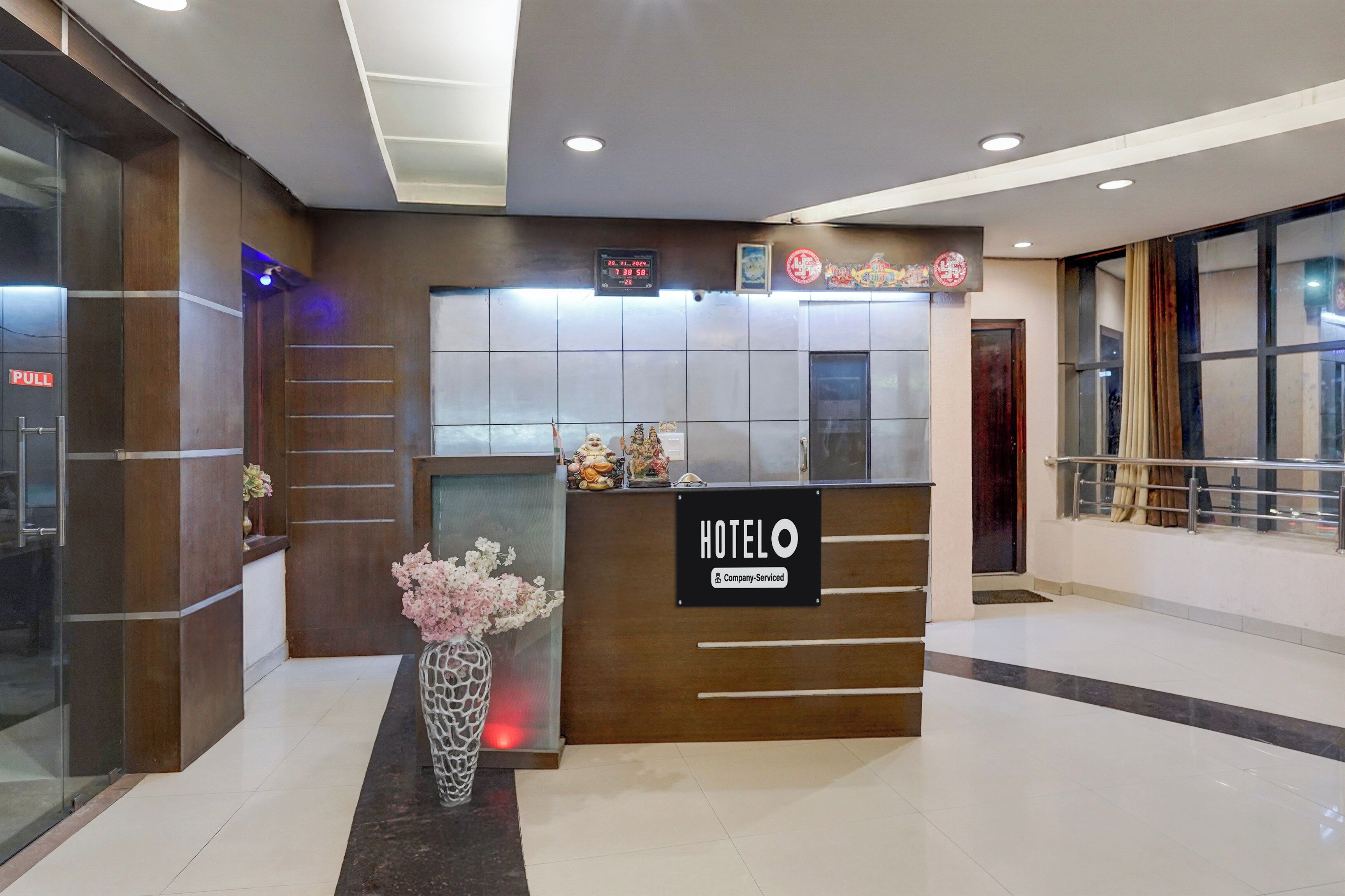 A hotel reception desk with a digital clock, a 'HOTEL' sign, and a vase with flowers.