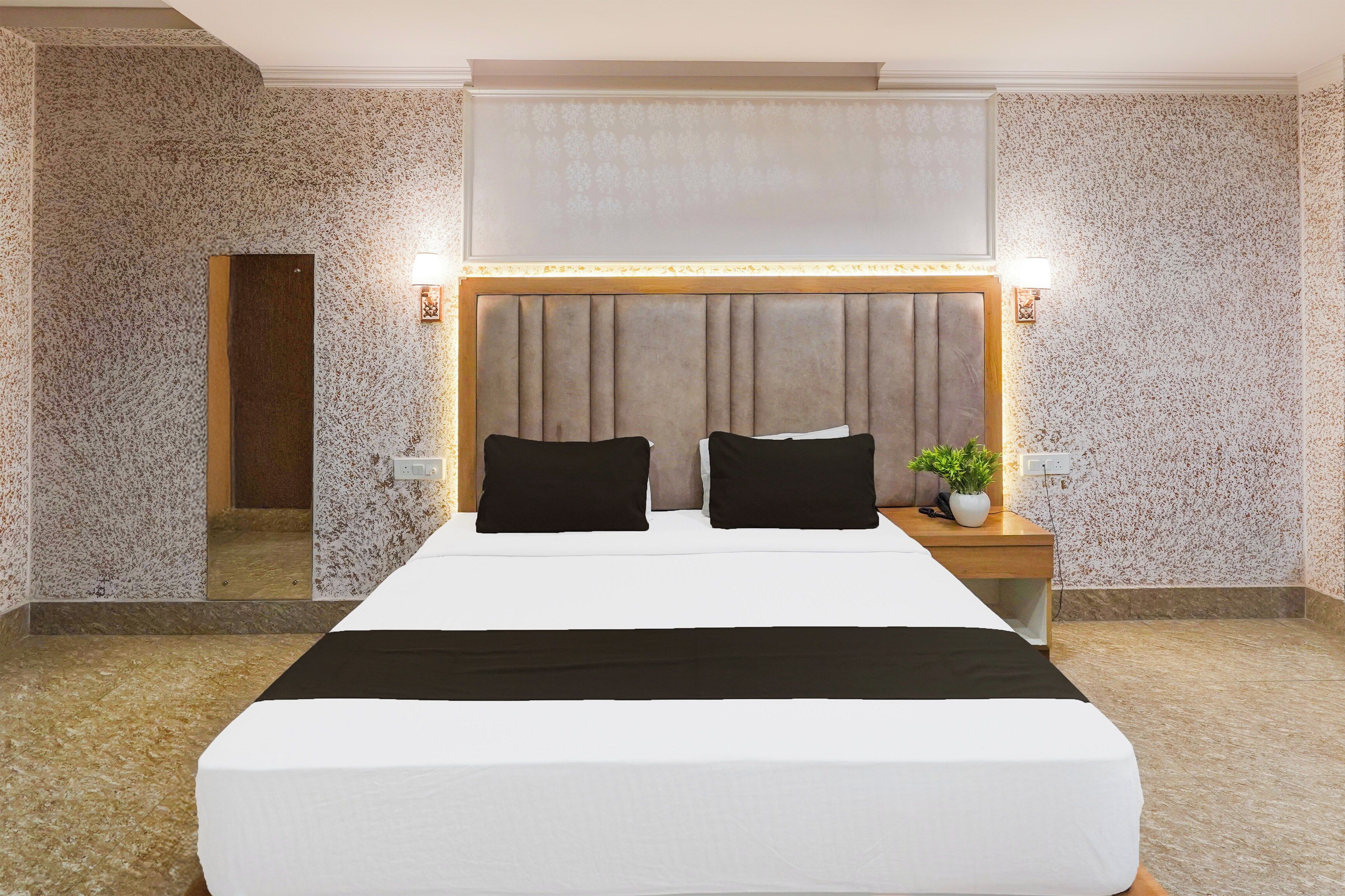 Una habitación de hotel con una cama grande, dos mesitas de noche, un espejo y una lámpara fijada a la pared.