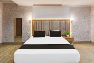 Una habitación de hotel con una cama grande, dos mesitas de noche, un espejo y una lámpara fijada a la pared.
