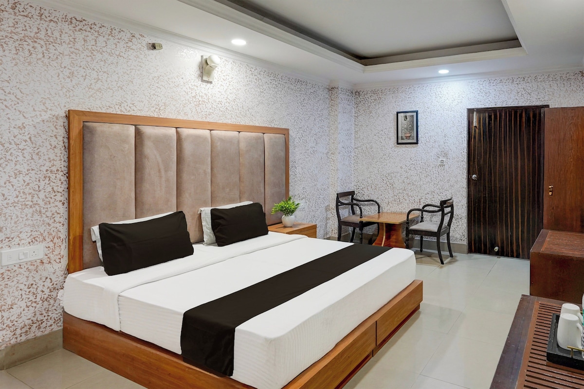A hotel room with a large bed, a wooden headboard, a small table with chairs, and a wardrobe.