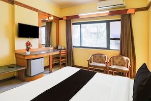Ein Hotelzimmer mit Bett, Schreibtisch, Stuhl, kleinem Kühlschrank, Fernseher und einem Fenster mit Vorhängen.