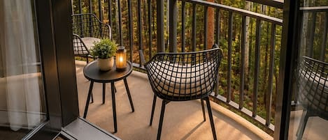 A balcony with a view of a forest, a table with a plant, and two chairs.