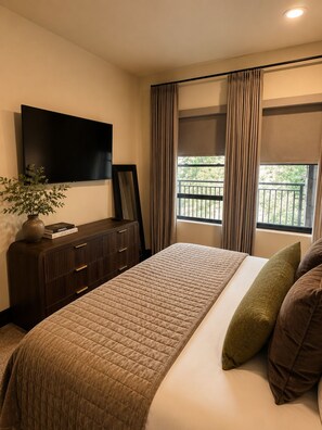 A hotel room with a large bed, a flat-screen TV mounted on the wall, a dresser, a potted plant, and a window with curtains. - Bear Creek Lodge 303a 1 Bedroom Condo (Telluride)