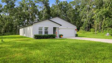 A single-story house with a garage, surrounded by a well-maintained lawn and dense trees.