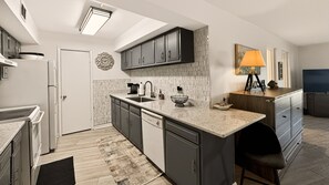 A modern kitchen with a central island, dark cabinets, and a tiled backsplash. - 525 El Matador 1 Bedroom Condo (Fort Walton Beach)