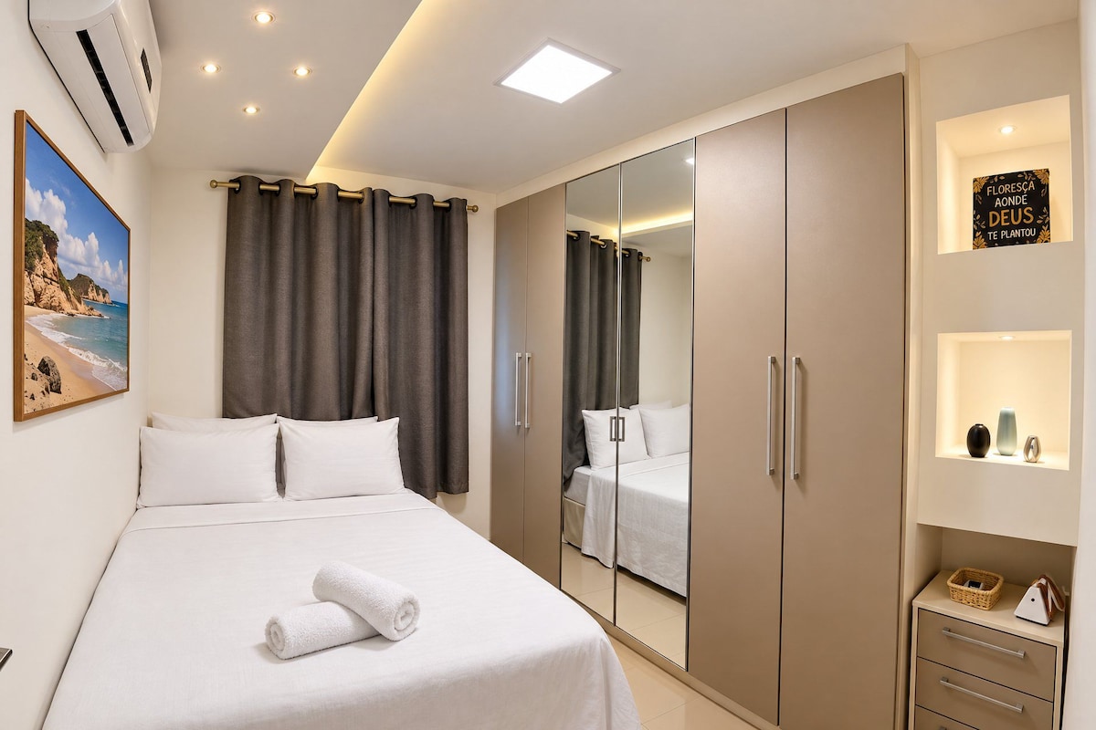A hotel room with a bed, a wardrobe, a mirror, and a shelf with decorative items.