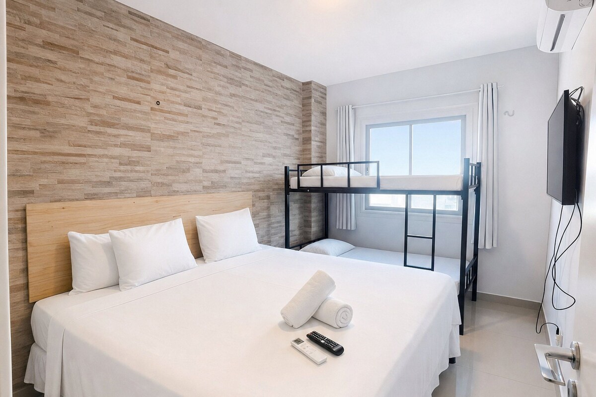 A hotel room with a large bed, a bunk bed, a television, and a window with curtains.