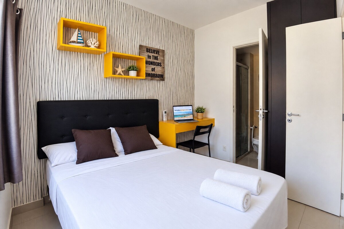 A hotel room with a bed, a desk, a chair, a door, and a wall with a striped pattern.