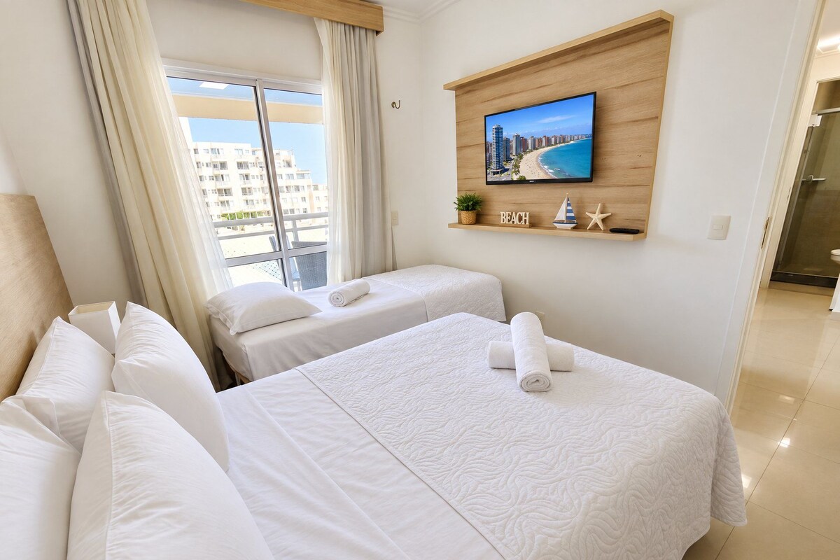 A hotel room with two beds, a large window with curtains, a television on the wall, and a view of the cityscape.