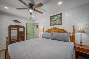 A bedroom with a bed, a nightstand, a lamp, a ceiling fan, a green door, and a fish mounted on the wall. - Sleeping Bear Cottage-a brand new getaway (Mentone)