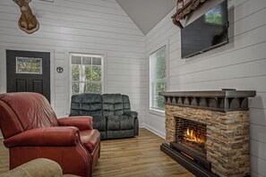 A room with a fireplace, two sofas, a television, and a door with a stained glass window. - Sleeping Bear Cottage-a brand new getaway (Mentone)