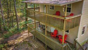 Een houten hut met twee verdiepingen en een balkon, omringd door bos.
