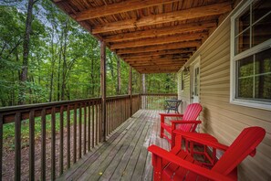 Eine Holzterrasse mit überdachtem Bereich, roten Adirondack-Stühlen und Blick auf einen Wald.