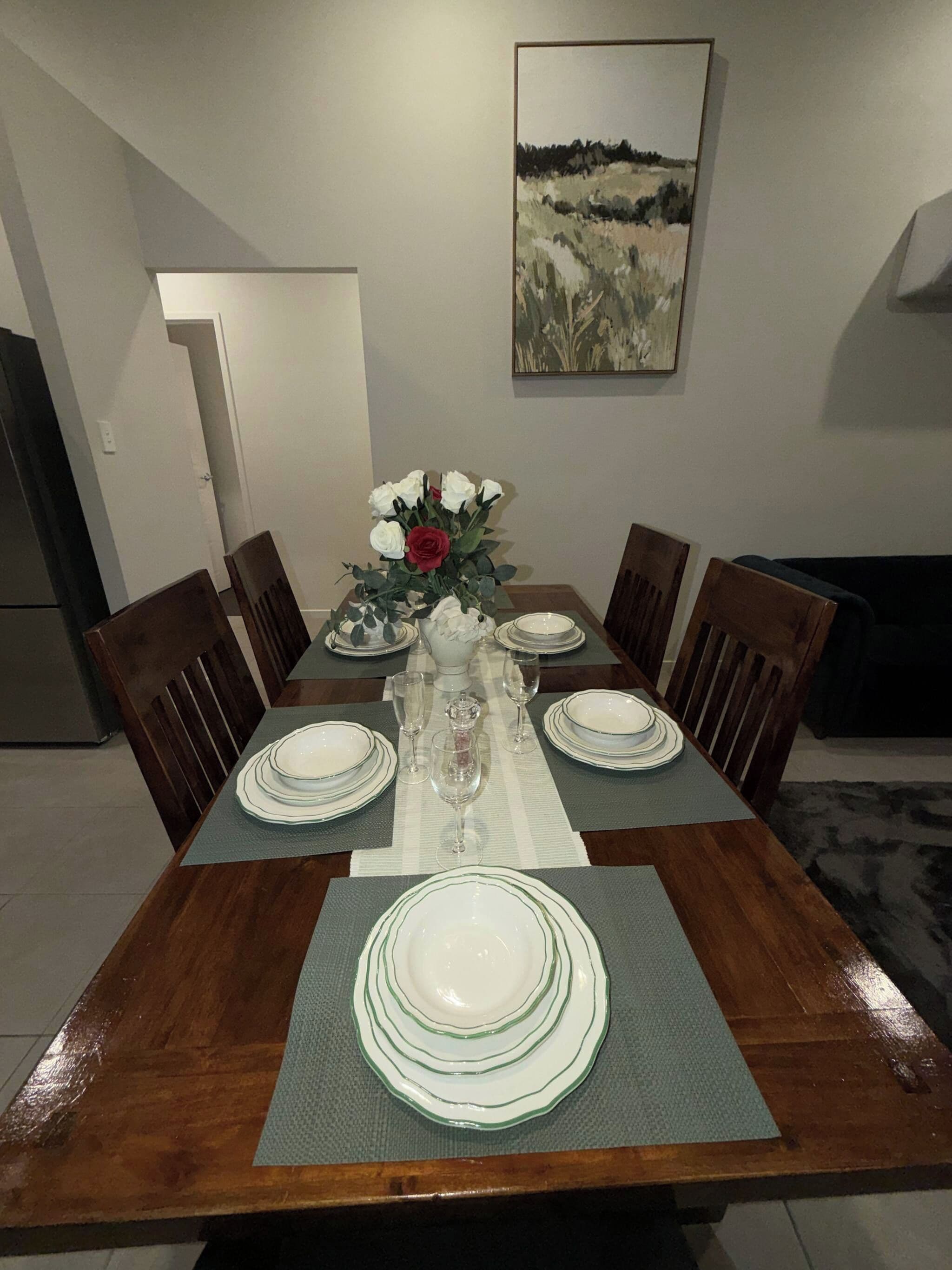 A dining table set with white plates, glasses, and a vase with flowers.