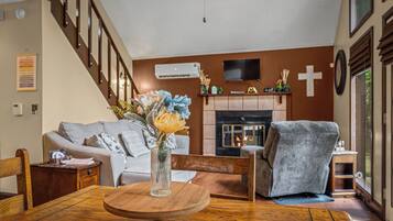 A living room with a fireplace, a sofa, a coffee table with a vase, and a staircase.