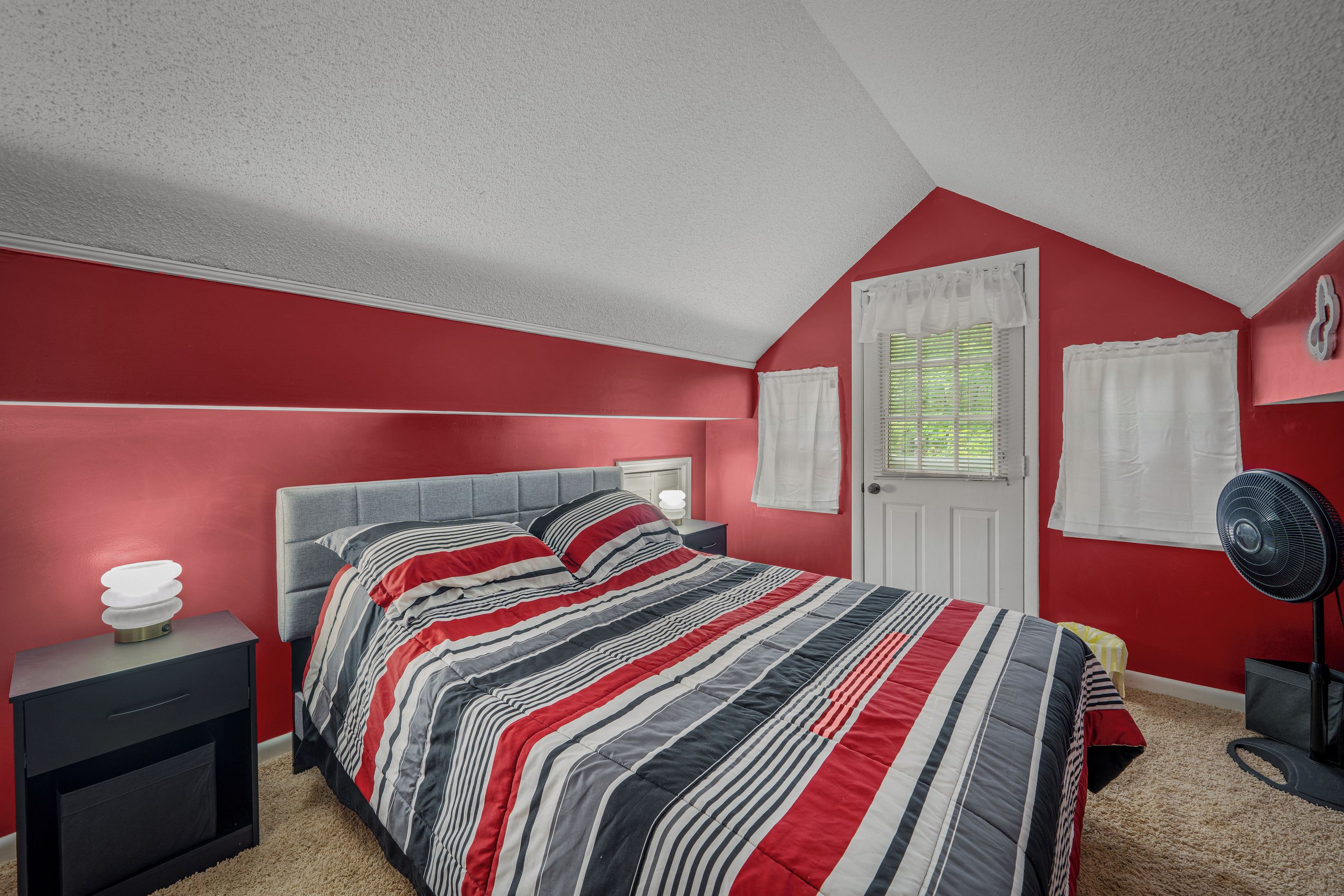 A bedroom with a bed, nightstand, and a standing fan.