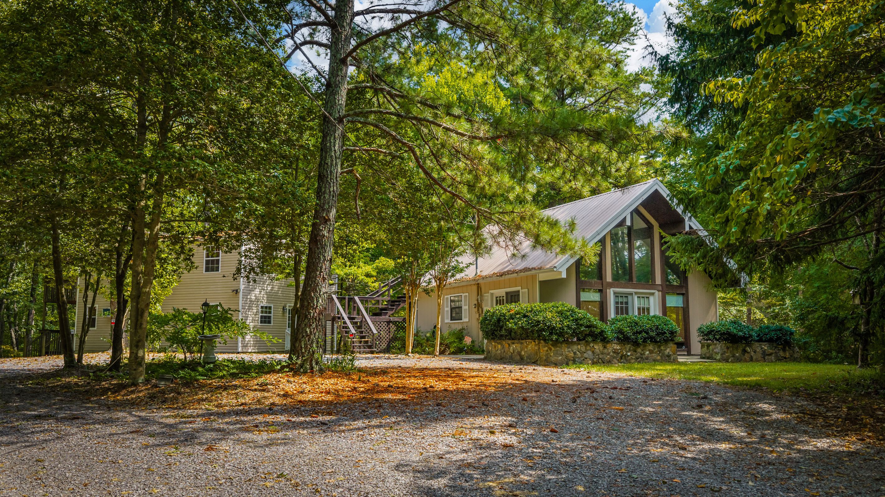 A two-story building with a stone foundation, surrounded by dense trees and a gravel driveway.