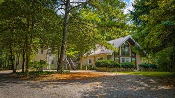 A two-story building with a stone foundation, surrounded by dense trees and a gravel driveway.