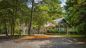 A two-story building with a stone foundation, surrounded by dense trees and a gravel driveway. - Cozy Cabin at Cash Cabins-sleep 5 (Mentone)