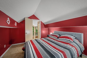 A bedroom with a bed, a red wall, and a door leading to another room. - Cozy Cabin at Cash Cabins-sleep 5 (Mentone)