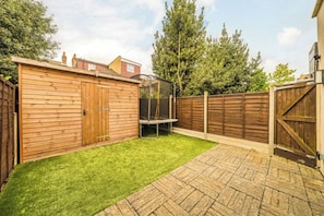 Un patio trasero con cerca de madera, un trampolín y césped verde.