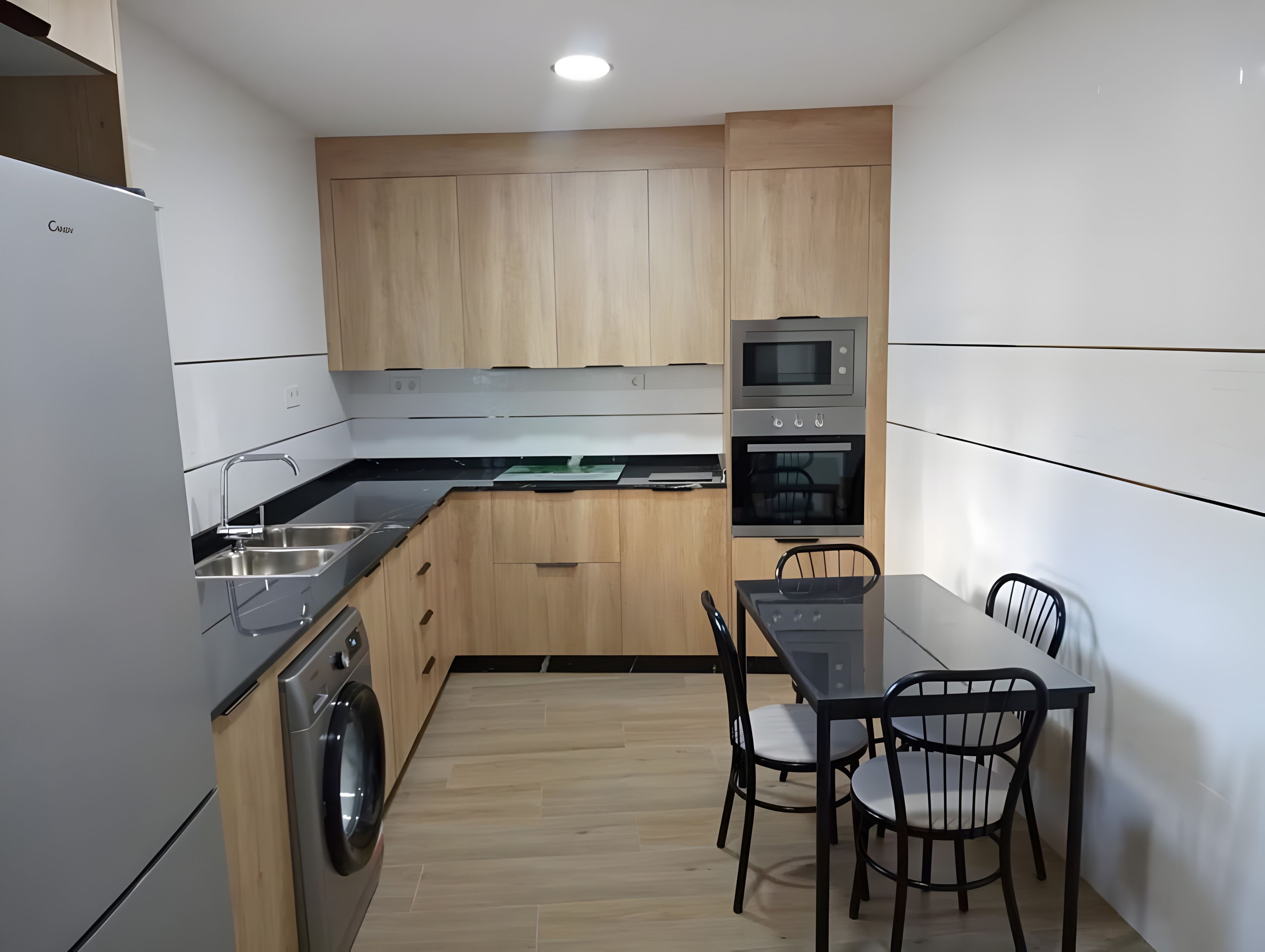 A compact kitchen with a washing machine, a microwave, and a dining area with chairs.