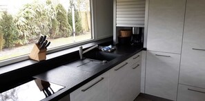 A modern kitchen with a black countertop, white cabinets, a window with a view of greenery, and a coffee maker. - Vacation home for 6 guests, 72 m², in Sankt Peter-Ording (318292) (Sankt Peter-Ording)